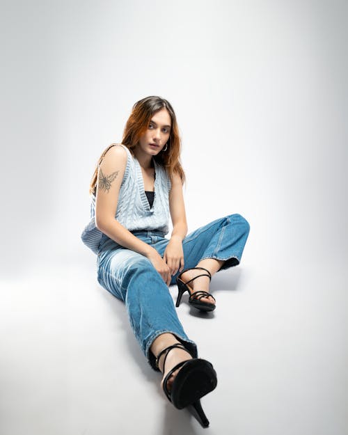 A woman in blue jeans and high heels sitting on the floor