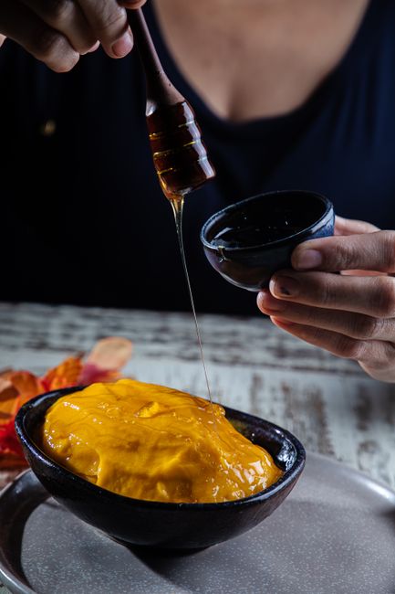 A bowl of smooth, deep-orange mango puree next to sliced ripe mango and a spoon coated in puree.