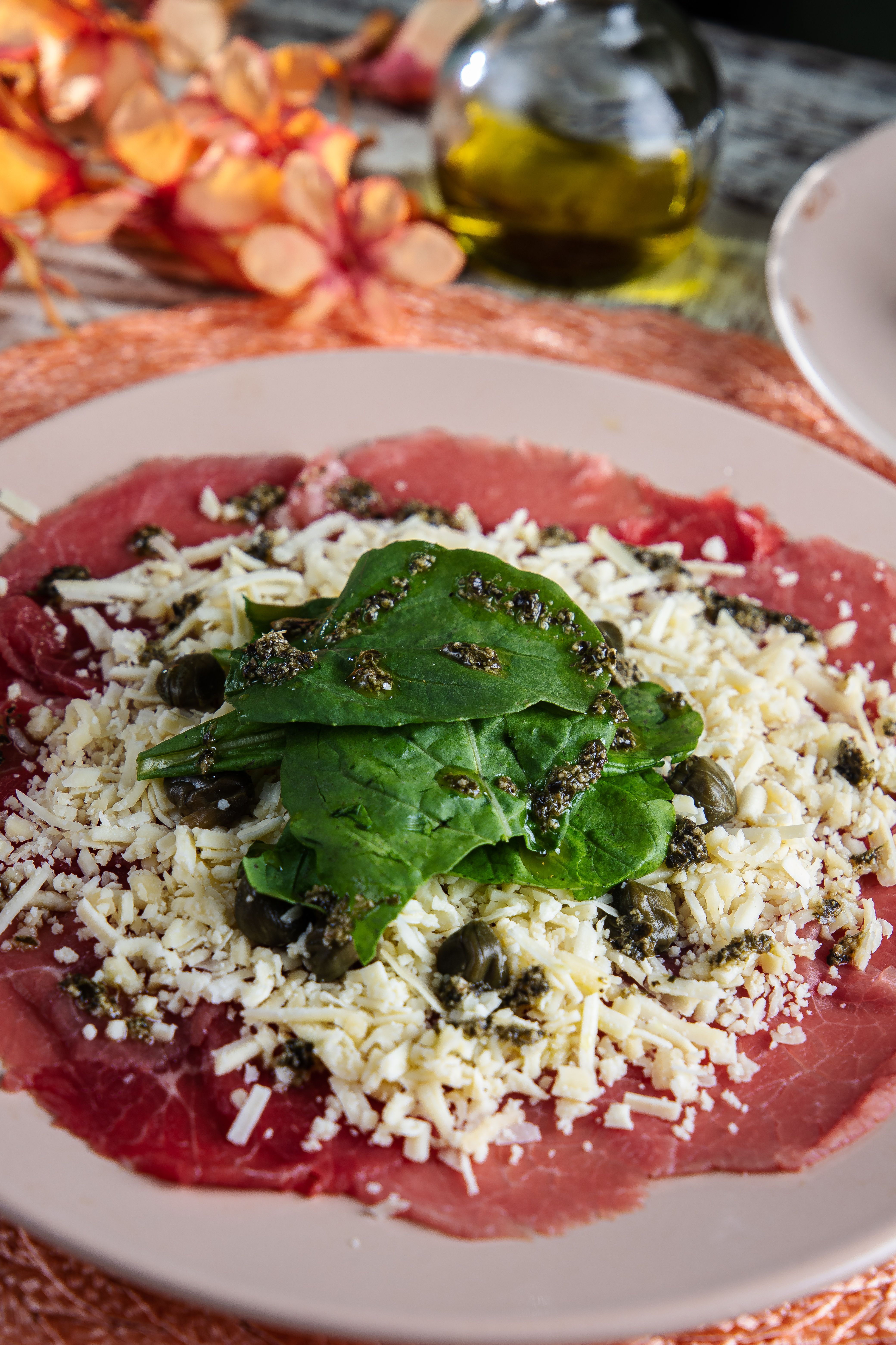 Close-up of classic beef carpaccio dish with paper-thin raw beef slices topped with parmesan and greens