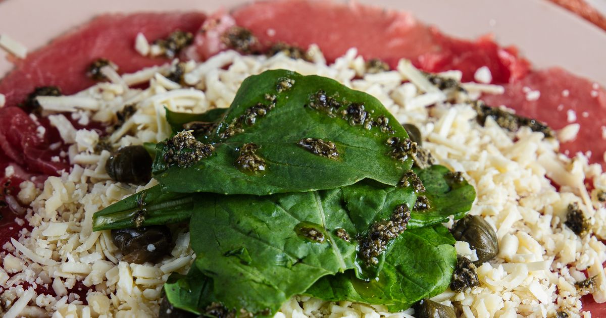 Close-up of classic beef carpaccio dish with paper-thin raw beef slices topped with parmesan and greens
