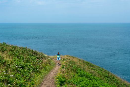 A lone hiker walking on a scenic grassy coastal trail with the ocean in the background.