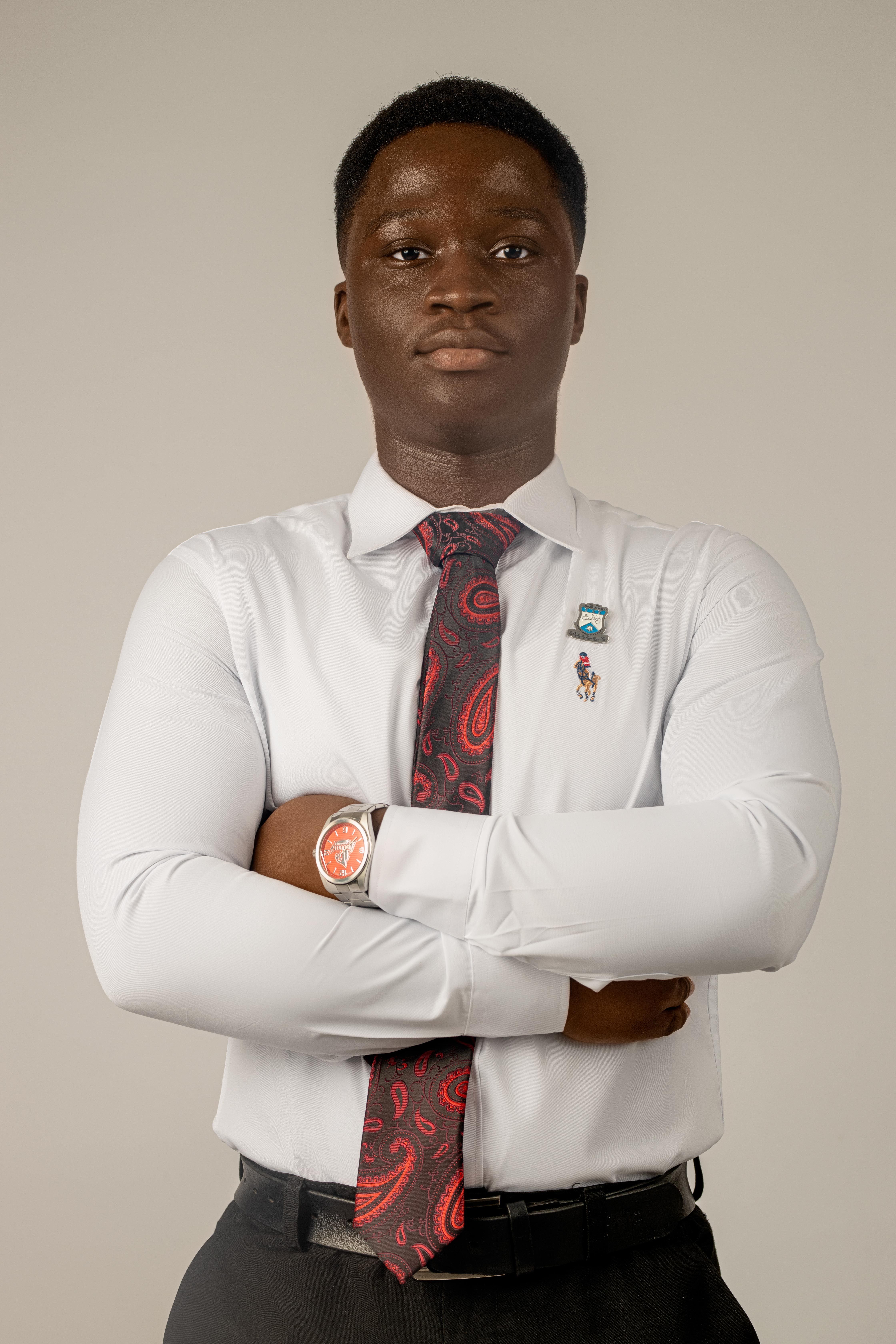 Portrait of a young man in a white shirt and tie, confidently crossing his arms.