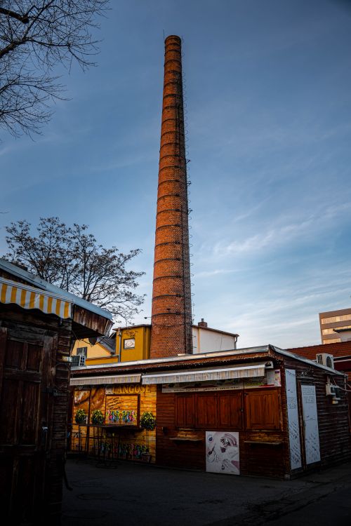 Free A tall brick chimney dominates the skyline in an urban industrial setting. Stock Photo