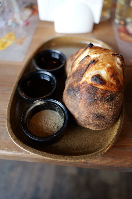 A dark, dense round slice of steamed brown bread being lifted from an open can, next to a bowl of baked beans
