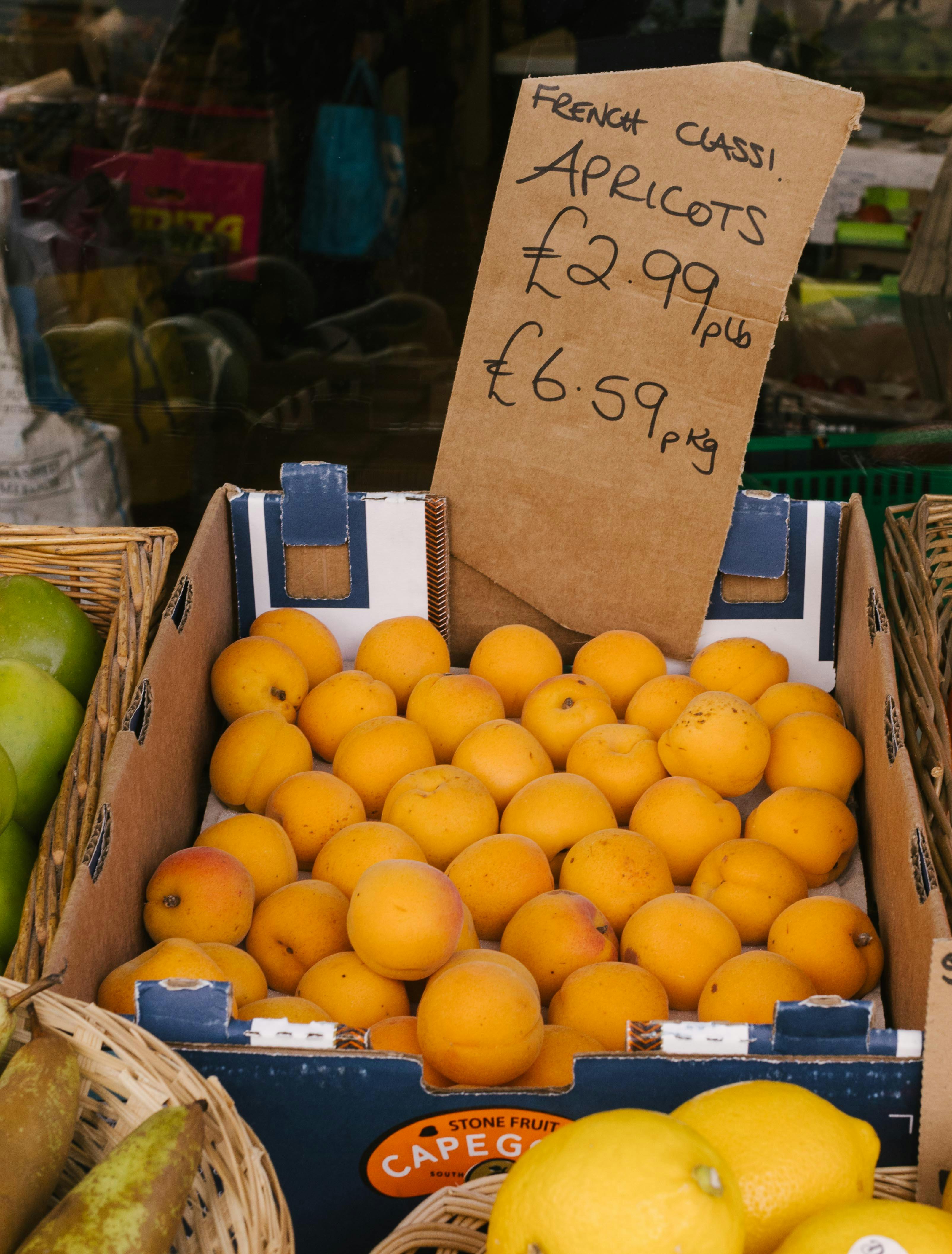 Box of fresh apricots and a price tag at a local market stall, inviting shoppers.