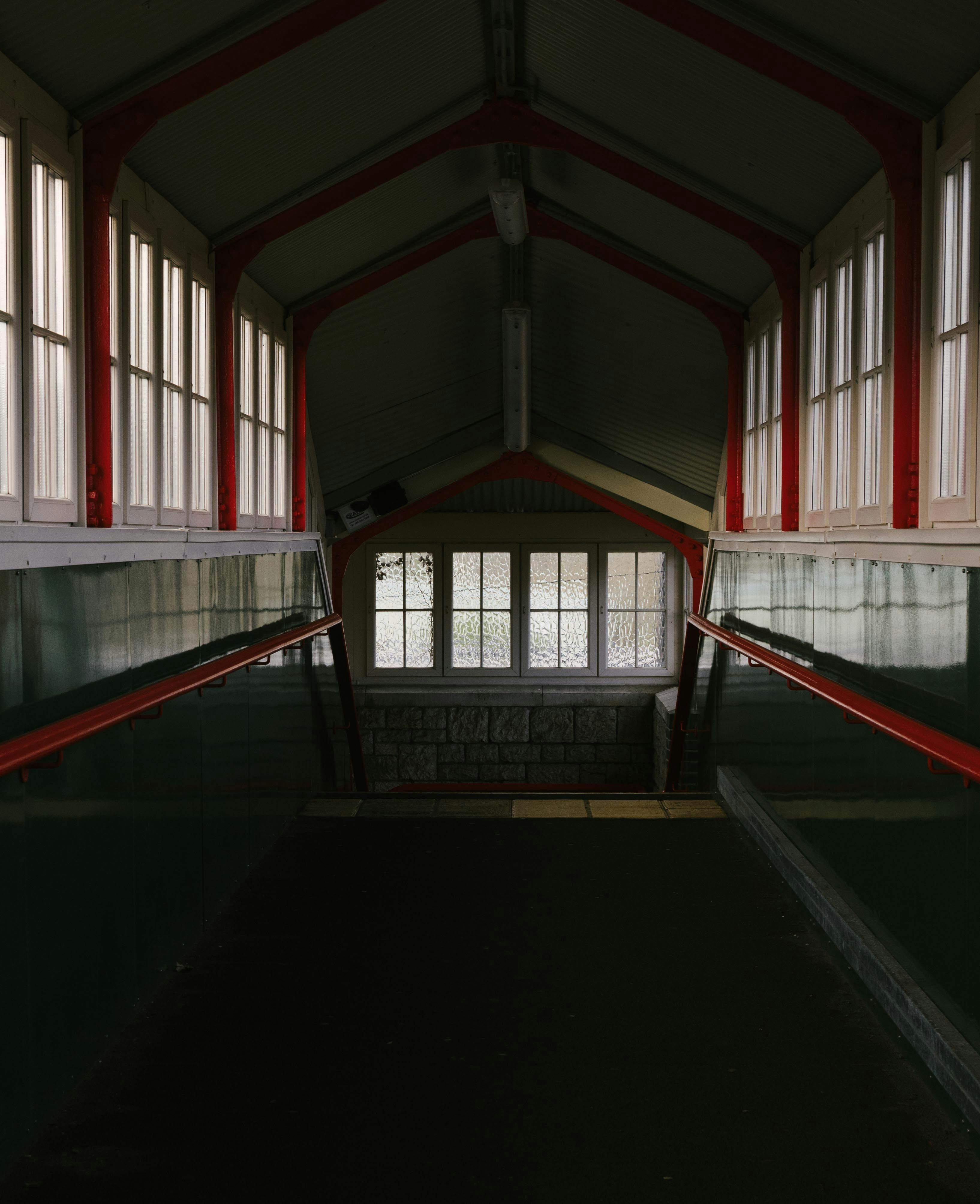 Dimly lit indoor staircase passage with vintage windows and handrails.