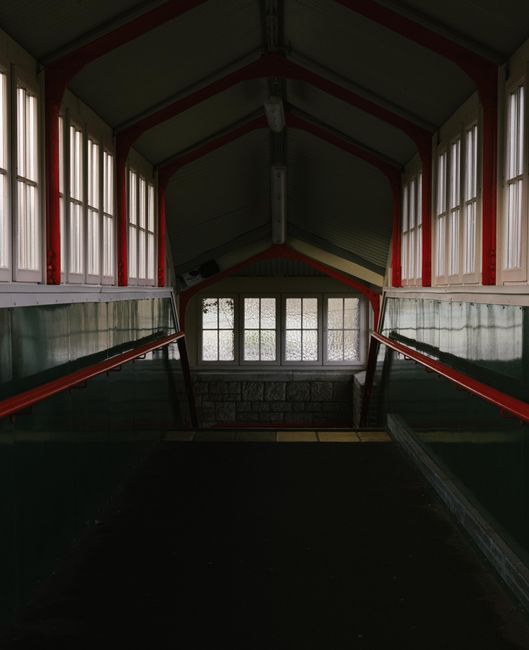 Dimly lit indoor staircase passage with vintage windows and handrails.