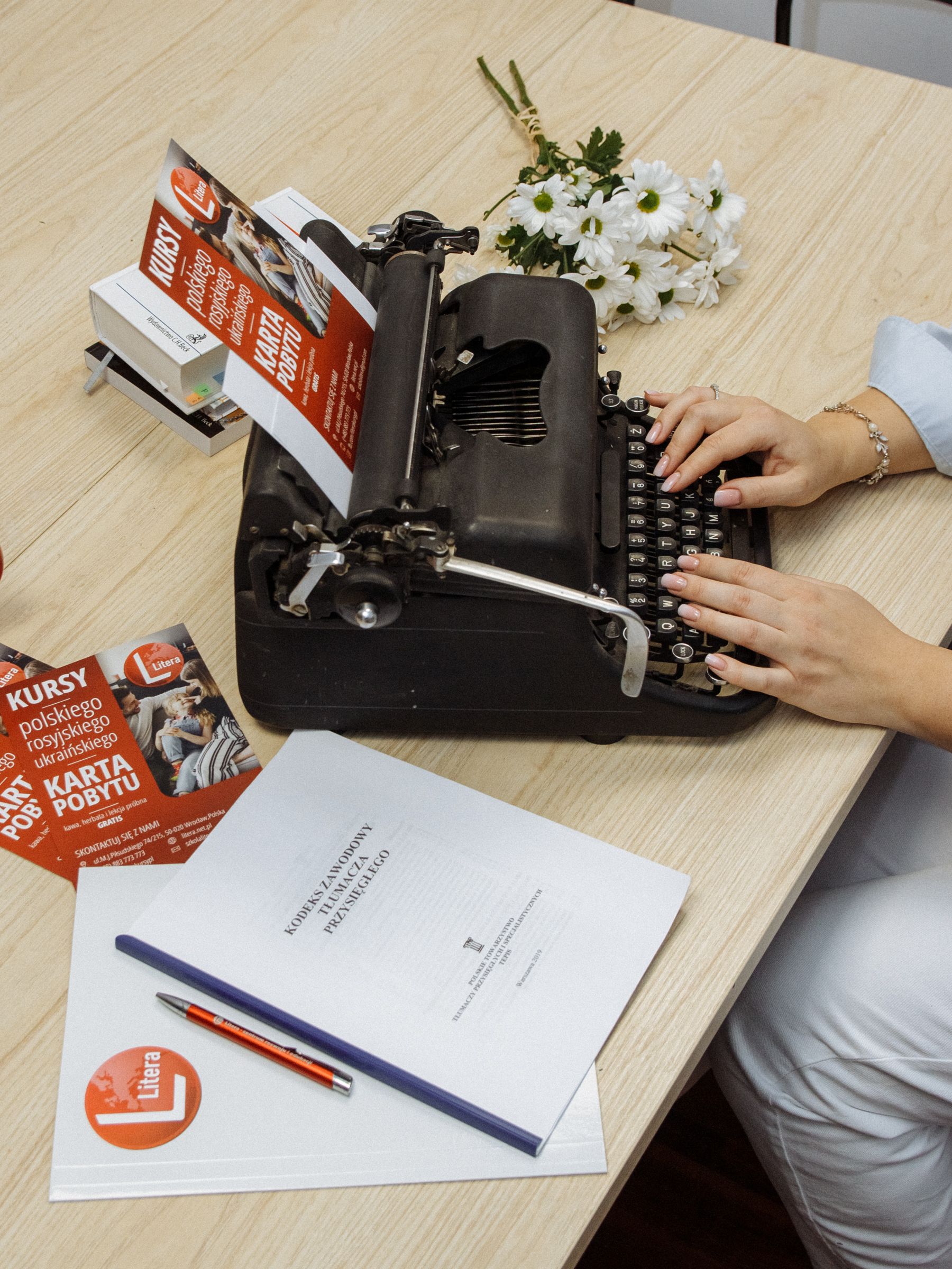 A woman typing on a vintage typewriter with documents and flowers on a desk.