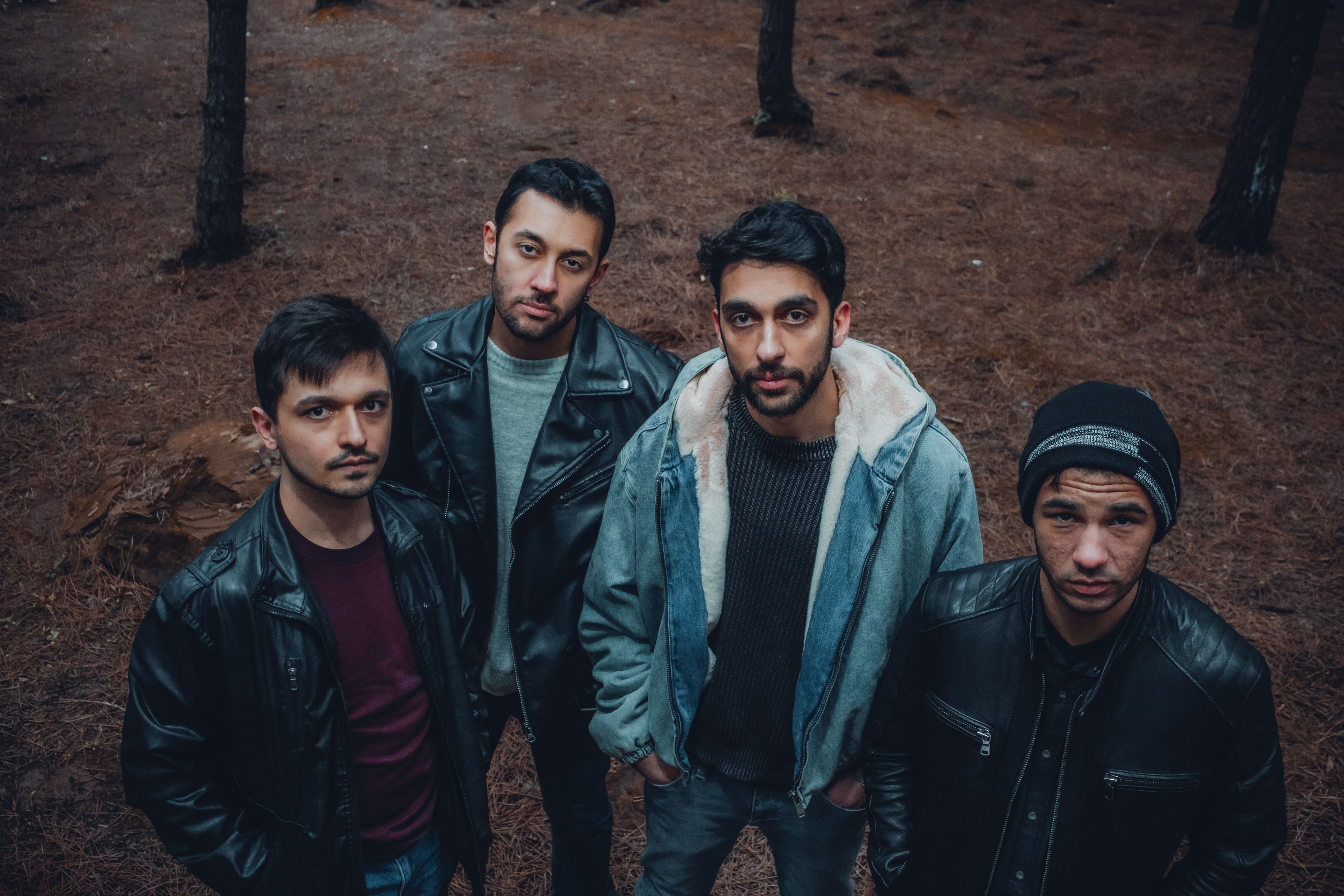 Four young men in jackets standing in a forest, captured from above.