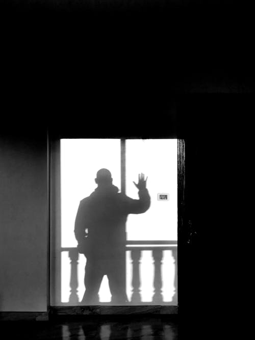 Man Standing with Arm Raised behind Window