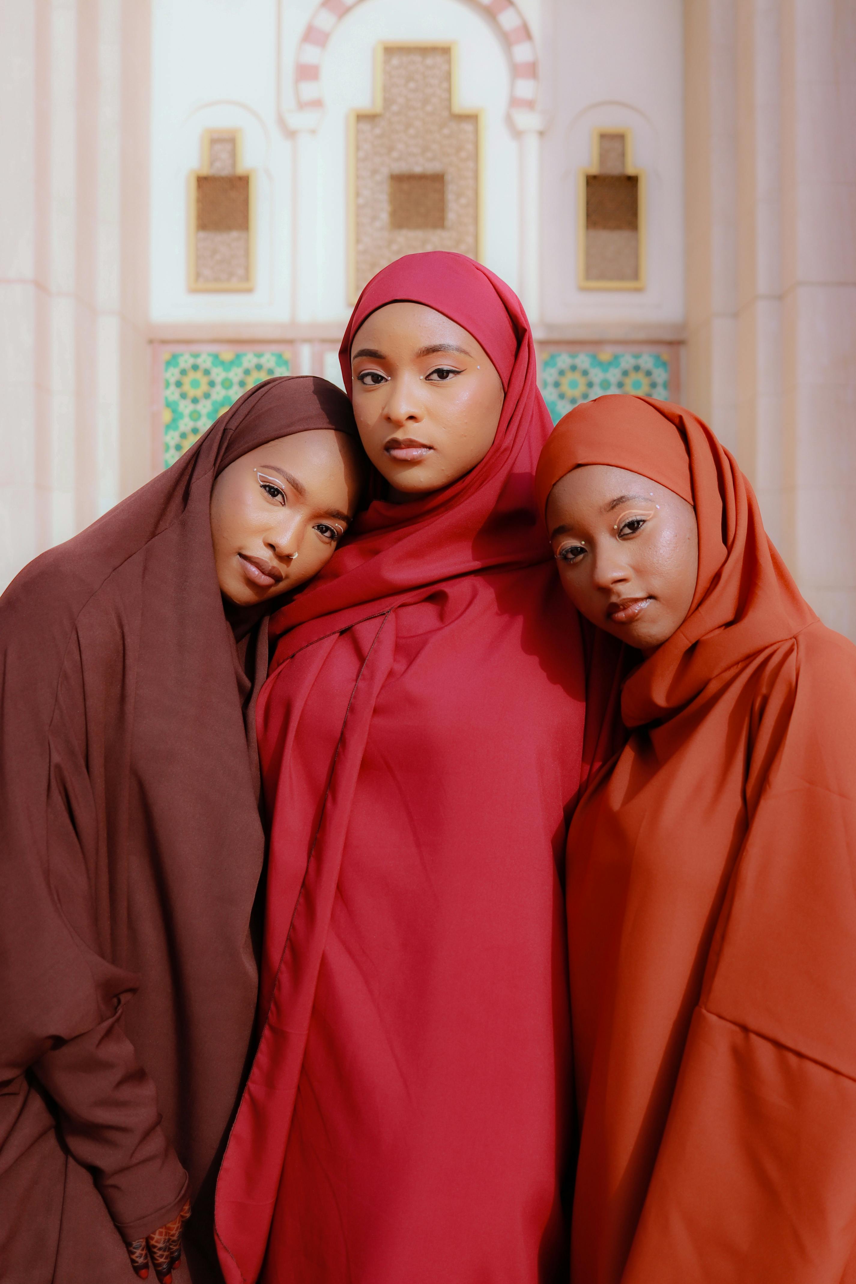 Three women in vibrant hijabs pose together against architectural backdrop.