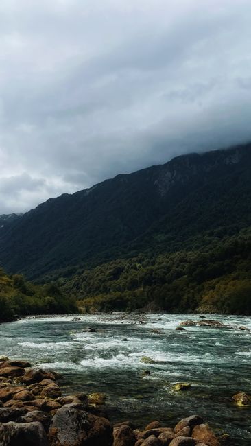 Fotomural Una vista impresionante de un río fluyendo a través de un paisaje montañoso exuberante bajo un cielo nublado.