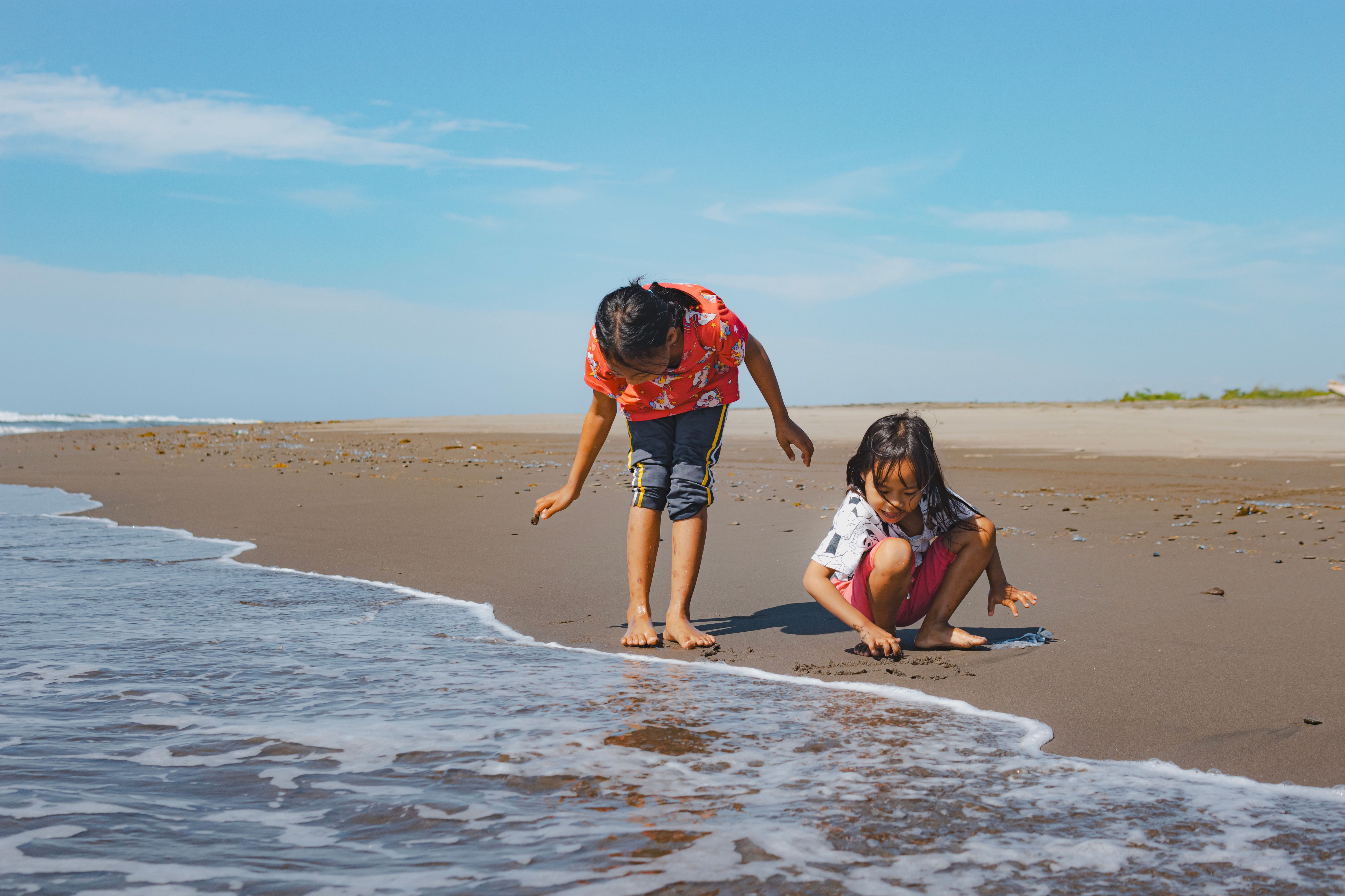 Two children enjoying beach play by the ocean on a sunny day.
