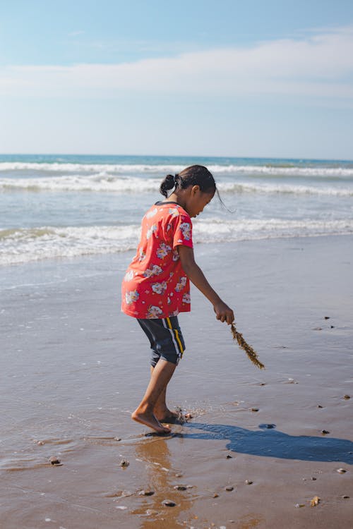 A little girl is playing on the beach with a stick
