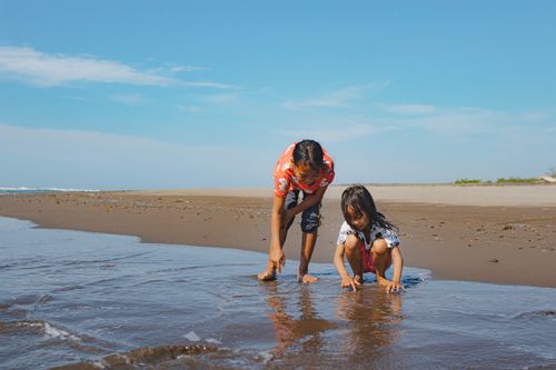 Free Two children enjoy a playful day at the beach, interacting with the water. Stock Photo