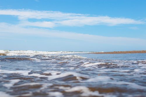 Free Calm ocean waves gently washing up on a sandy beach under a bright blue sky. Stock Photo