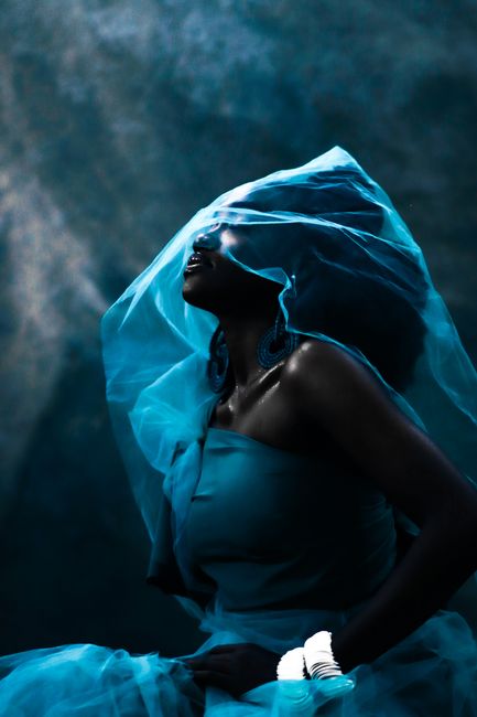 Artistic portrait of a woman draped in blue fabric, captured in moody lighting.