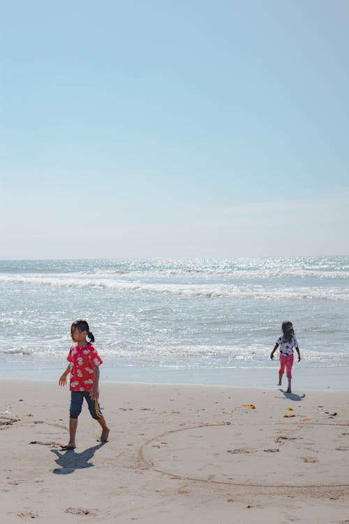 Free Two children running on the beach with the ocean in the background Stock Photo