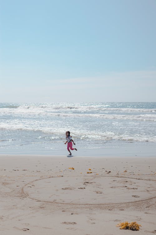 A child running on the beach with a heart drawn in the sand