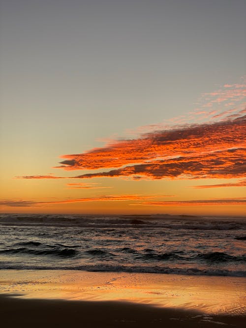 A sunset over the ocean with a beach and a surfboard