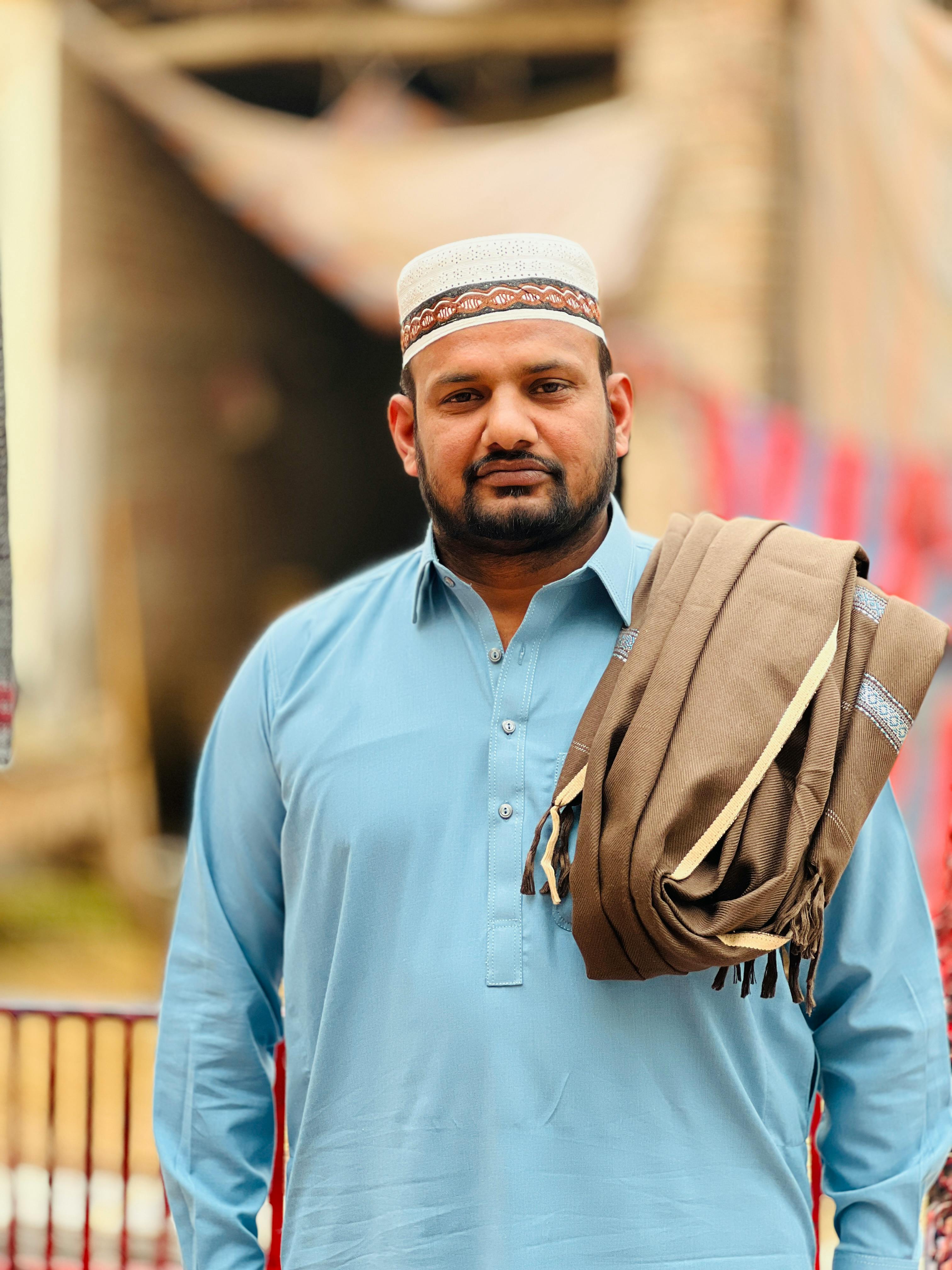 Portrait of a man in traditional clothing with a hat and shawl in an outdoor setting.