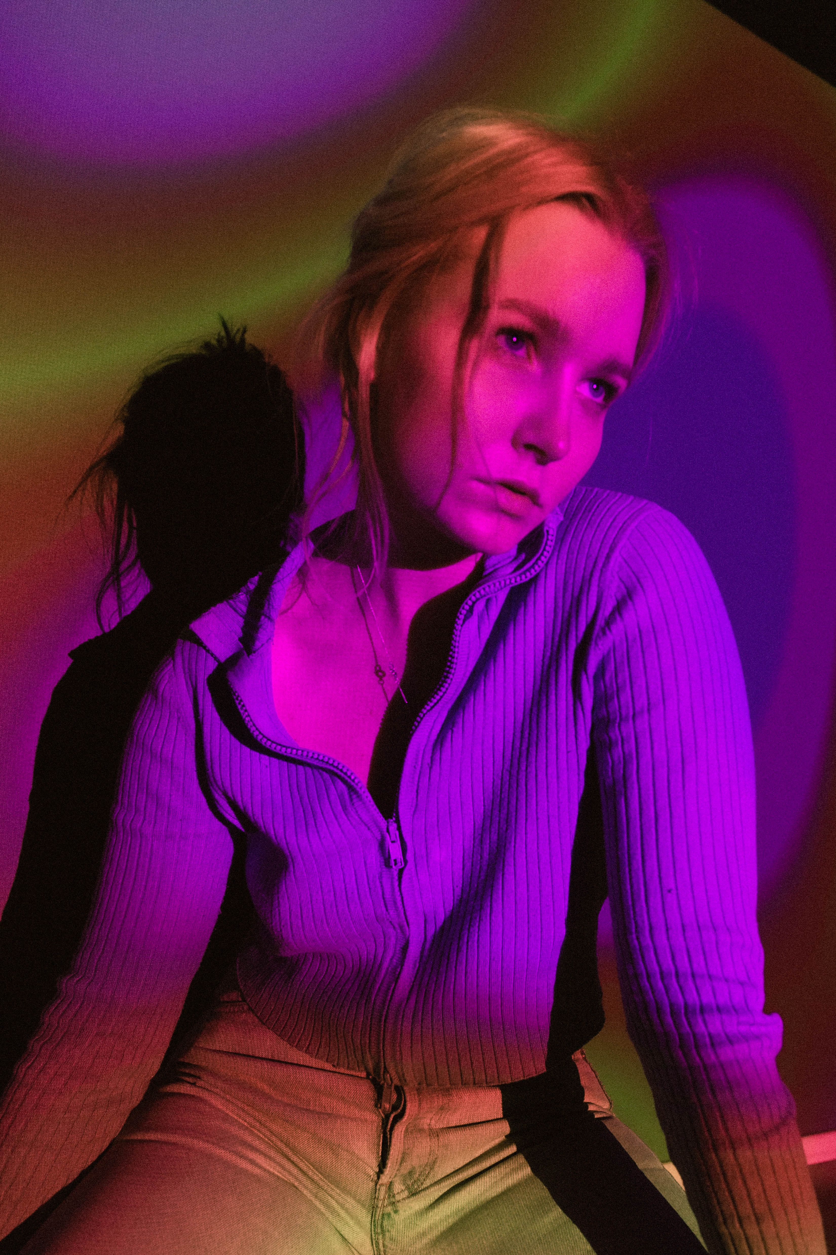 Young woman in a sweater posed under colorful purple lighting. Artistic portrait photography.
