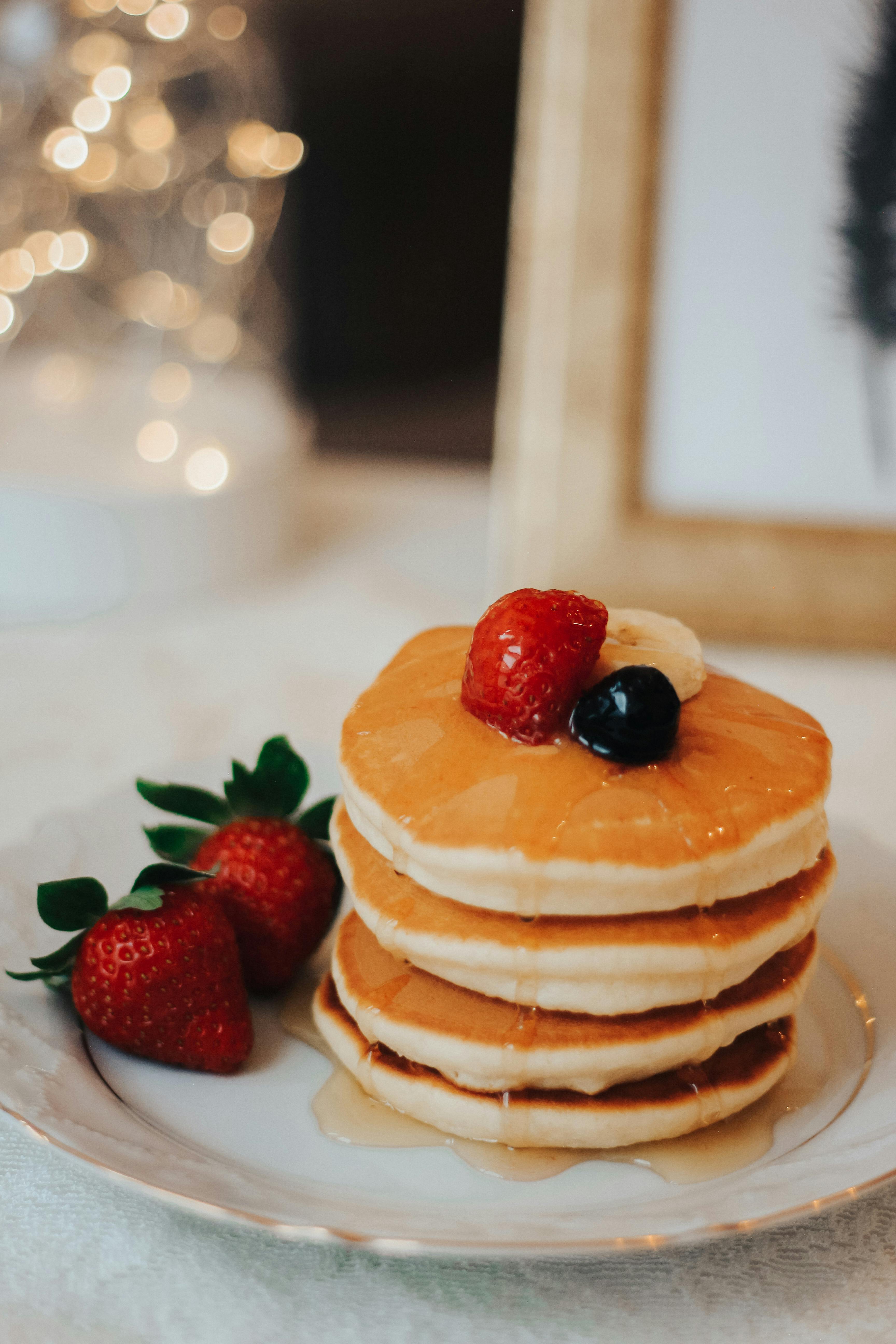 A mouthwatering stack of pancakes topped with strawberries and syrup, perfect for a cozy breakfast.