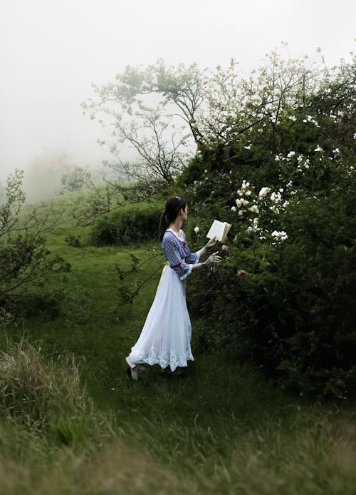 character standing in wedding gown holding a book in hand near meadows | lostintespace • by Amaan