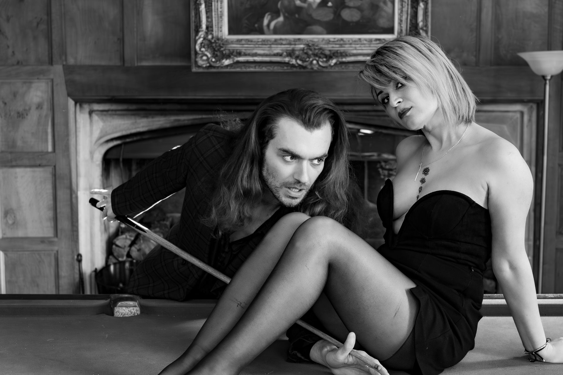 A couple in a romantic black and white setting on a pool table indoors.