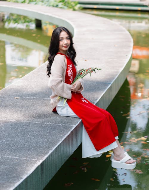 Pretty Woman in Red Dress Sitting by Pond in Park