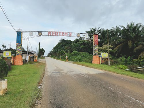 A gate with the text 'Felda Kerteh 3' under a cloudy sky near an area of villages and oil palm plantations.