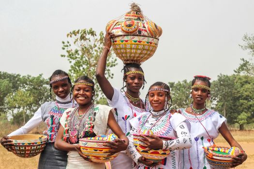Group of women in traditional attire holding colorful ceramic pots outdoors.