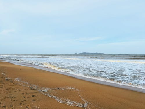 A view of a calm beach with wind waves hitting the beach in the monsoon season and cloudy skies.