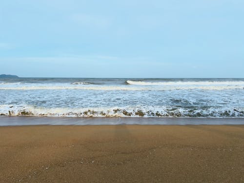 A view of a calm beach with wind waves hitting the beach in the monsoon season and cloudy skies.