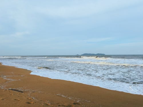 A view of a calm beach with wind waves hitting the beach in the monsoon season and cloudy skies