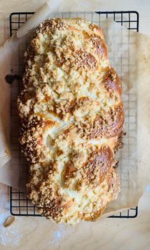 Freshly baked challah with streusel topping on parchment paper and cooling rack.