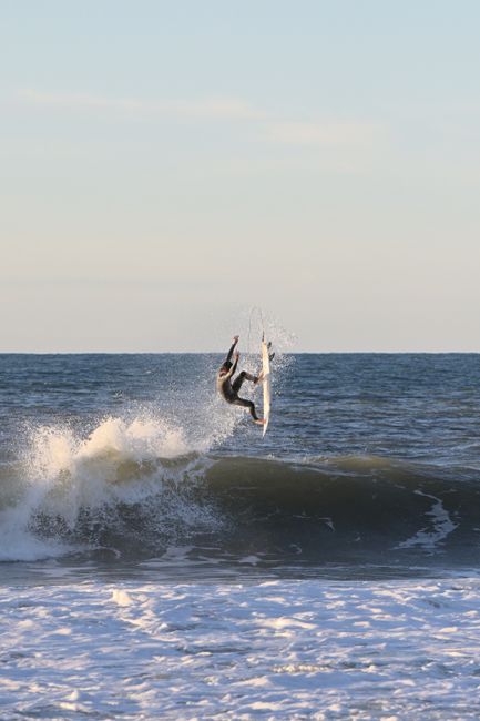 Surfer performing an aerial maneuver on a wave, showcasing skill and thrill of surfing adventure.