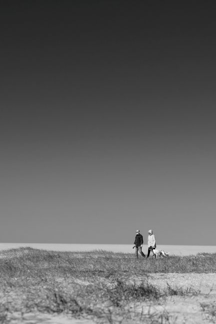A scenic black and white photo of a couple walking their dog on Foz do Arelho beach.