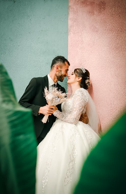 A bride and groom are standing in front of a colorful wall