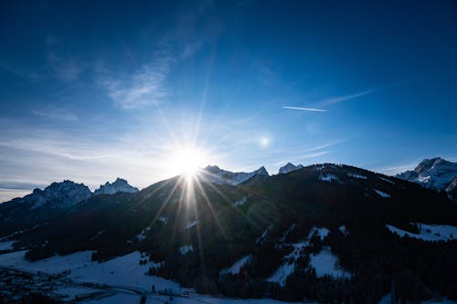 The sun shines brightly over a snowy mountain range