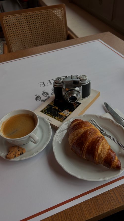 Free A cozy breakfast scene featuring coffee, croissant, and vintage camera on a table. Stock Photo
