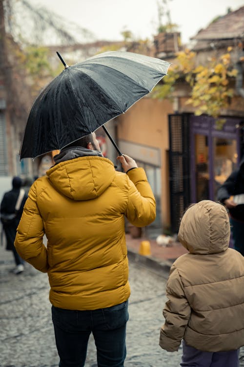 A man and a child are walking down a street with an umbrella