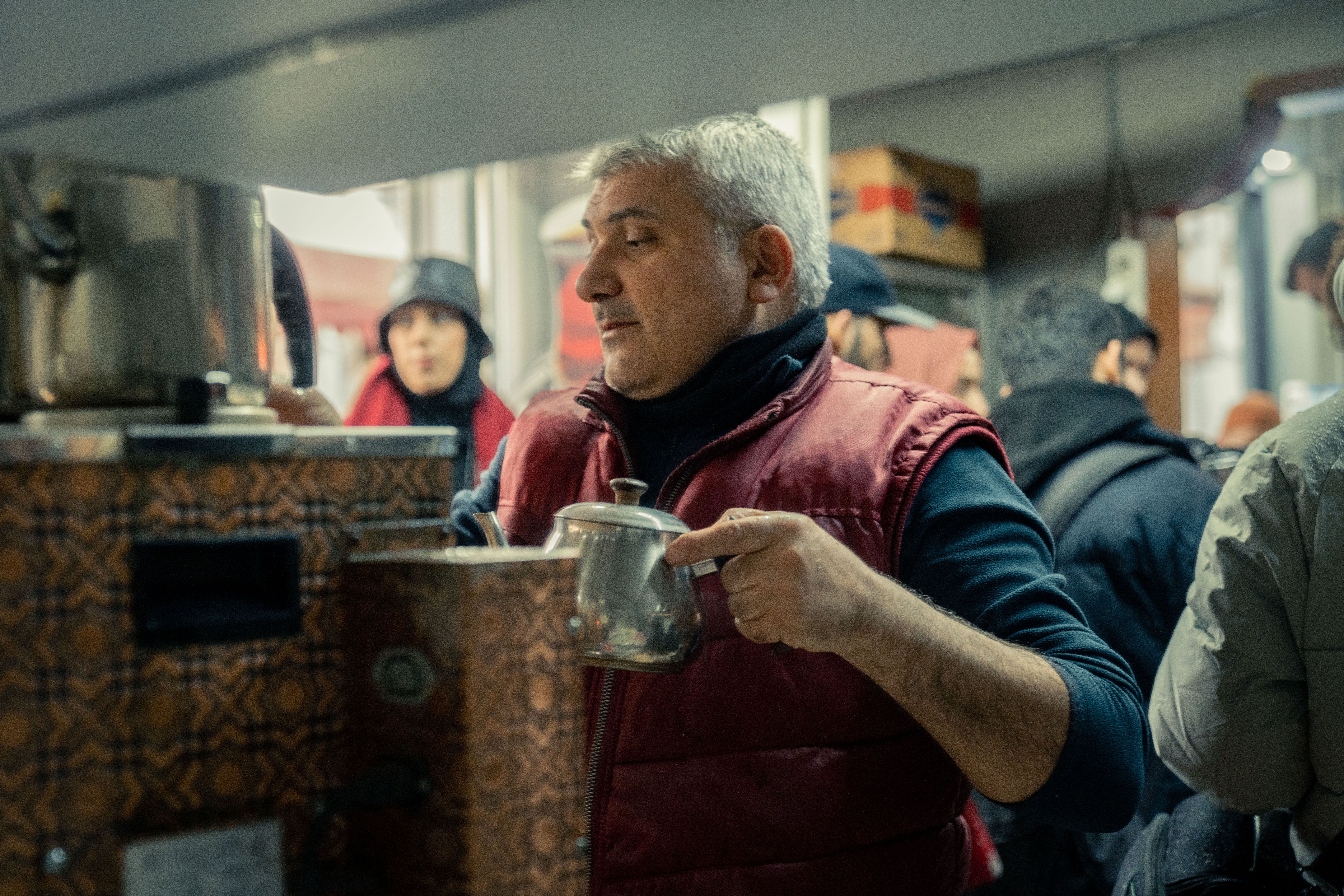 茶器を持つ高齢の男性が周囲の人々とともに賑やかな都市環境にいる。