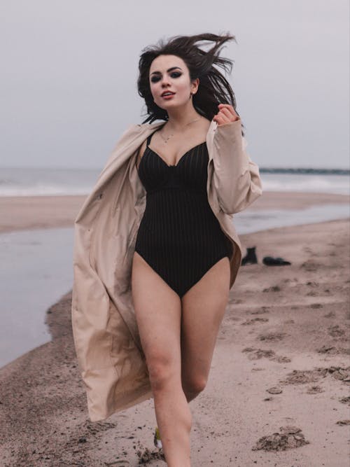 Free Woman in Trench and Bodysuit Running on Beach Stock Photo