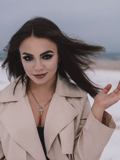 Free Elegant woman with dark makeup poses in a trench coat on a winter beach. Stock Photo