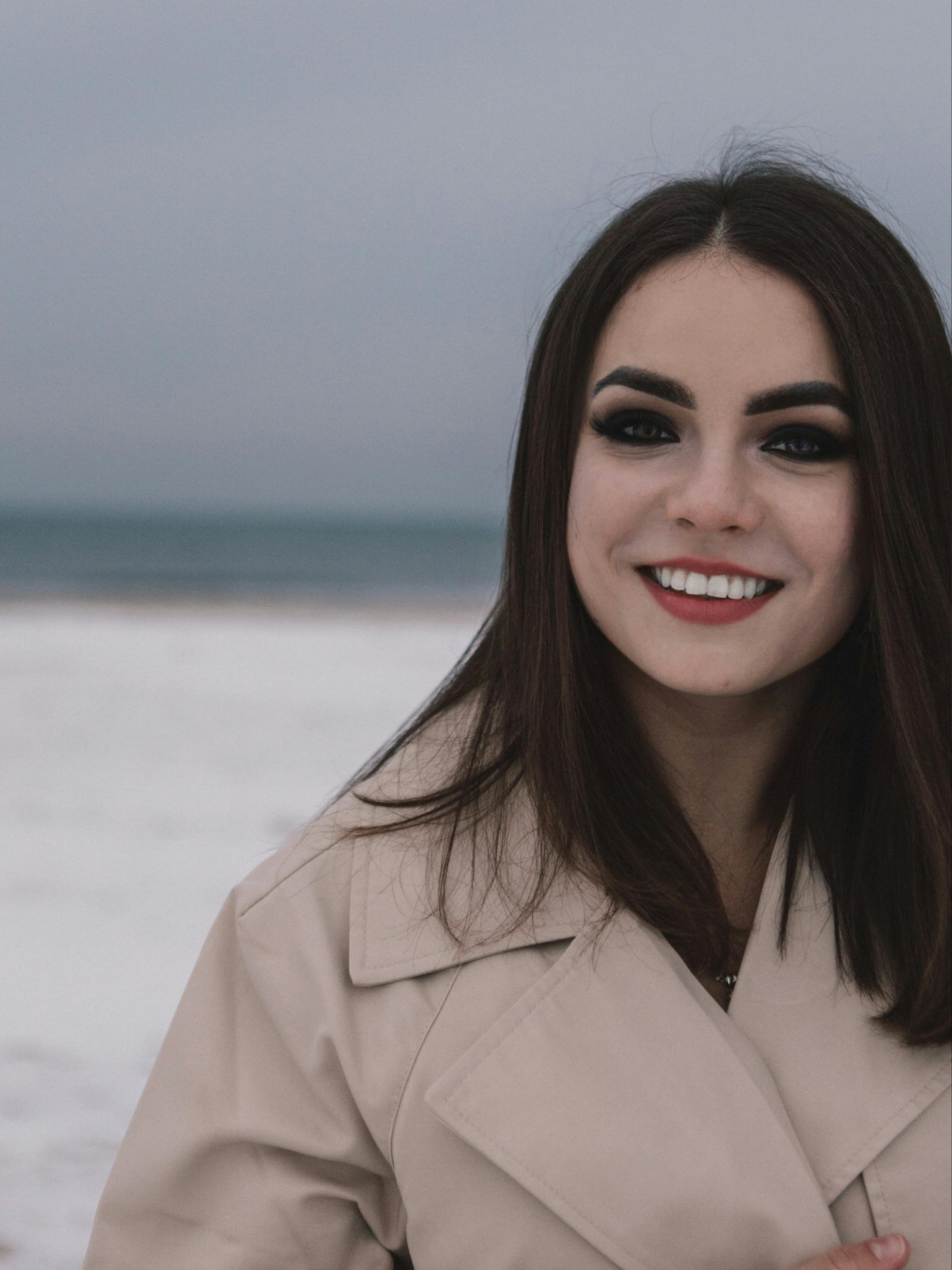 Young woman in a beige coat smiling by the cold winter seaside.
