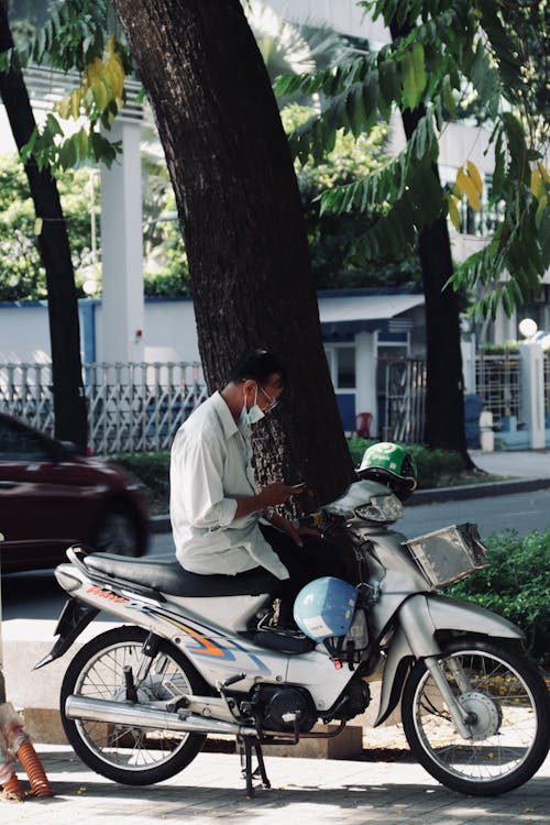 Candid Photo of a Man Sitting on a Motor Scooter on a Street in City 