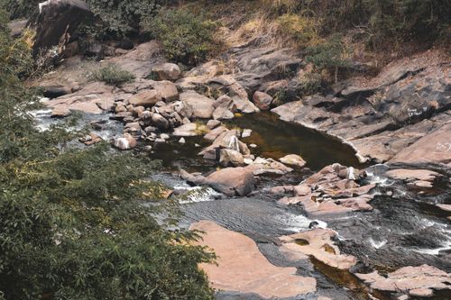 Free Peaceful stream flowing through rocky terrain with surrounding greenery and eroded stones. Stock Photo