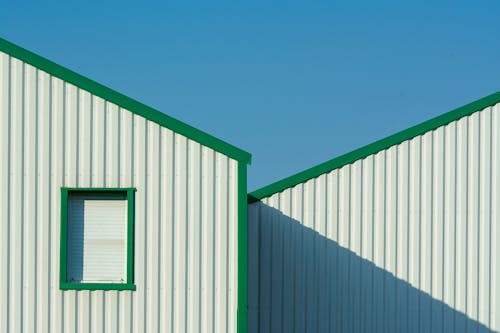Two metal buildings with green windows and a blue sky