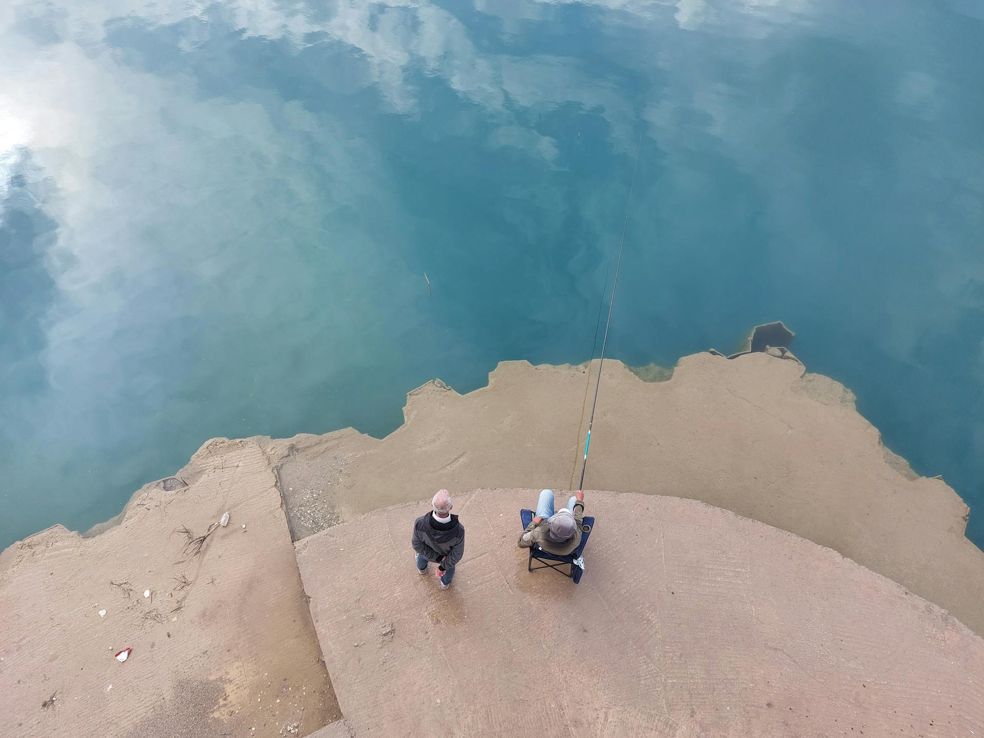 Two men fishing from a concrete shore, enjoying a peaceful day by the water.